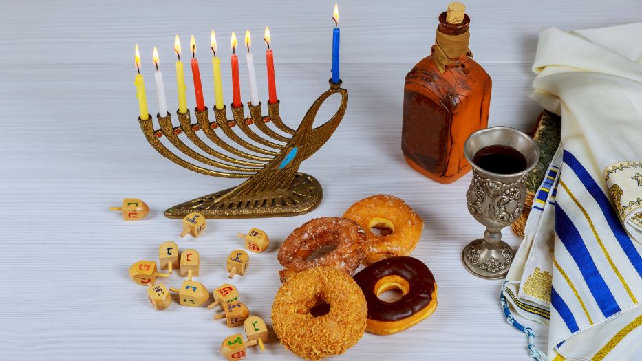 Bagels, Gebetsschal, neunarmiger Hanukkah-Leuchter und Weinkelch stehen auf einem Tisch 