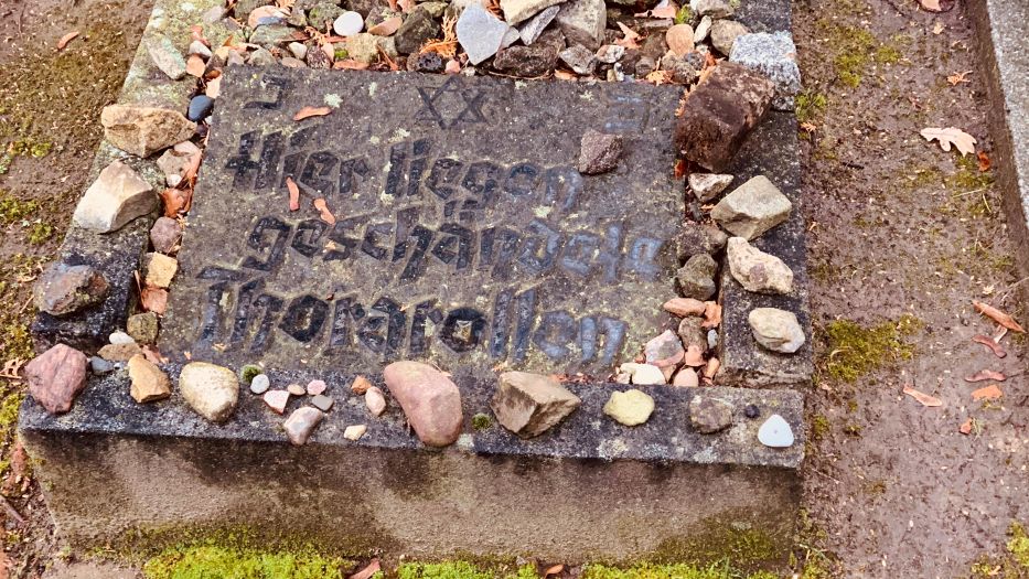 Gedenkstein auf jüdischem Friedhof mit der Inschrift: „Hier liegen geschändete Thorarollen“ mit kleinen Steinen darauf